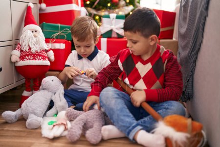 Foto de Dos niños jugando con juguetes sentados en el suelo junto al árbol de Navidad en casa - Imagen libre de derechos