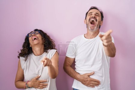 Téléchargez les photos : Couple hispanique du moyen âge ensemble sur fond rose riant de vous, pointant du doigt l'appareil photo avec la main sur le corps, expression de honte - en image libre de droit
