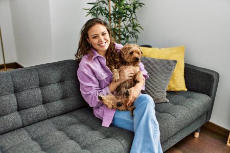 Téléchargez les photos : Jeune belle femme hispanique étreignant chien assis sur le canapé à la maison - en image libre de droit