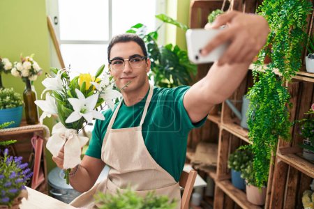 Photo for Young hispanic man florist make selfie by smartphone holding flowers at flower shop - Royalty Free Image