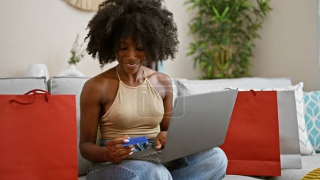 Téléchargez les photos : Femme afro-américaine utilisant un ordinateur portable et des achats par carte de crédit à la maison - en image libre de droit