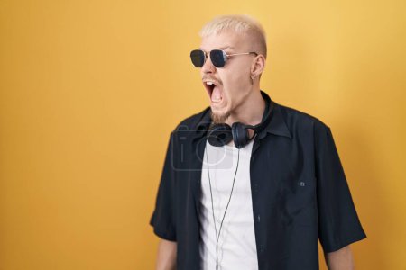 Photo for Young caucasian man wearing sunglasses standing over yellow background angry and mad screaming frustrated and furious, shouting with anger. rage and aggressive concept. - Royalty Free Image