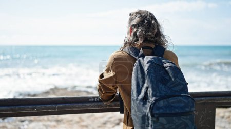 Téléchargez les photos : Jeune homme hispanique touriste portant un sac à dos debout à l'envers au bord de la mer - en image libre de droit