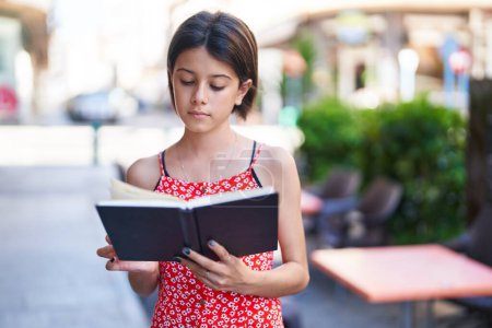 Photo for Adorable hispanic girl reading book at street - Royalty Free Image