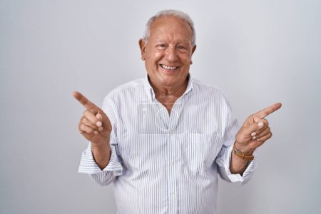 Téléchargez les photos : Homme âgé avec les cheveux gris debout sur fond isolé souriant confiant pointant avec les doigts vers différentes directions. espace de copie pour la publicité - en image libre de droit