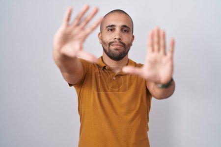 Téléchargez les photos : Homme hispanique avec barbe debout sur fond blanc faisant cadre à l'aide de mains paumes et doigts, perspective de la caméra - en image libre de droit