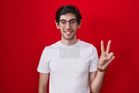 Photo for Young hispanic man standing over red background showing and pointing up with fingers number two while smiling confident and happy. - Royalty Free Image