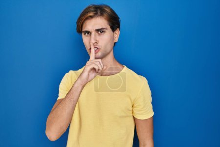 Photo for Young man standing over blue background asking to be quiet with finger on lips. silence and secret concept. - Royalty Free Image