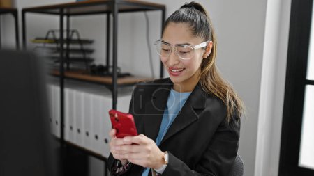 Téléchargez les photos : Jeune belle hispanique travailleuse d'entreprise utilisant un smartphone travaillant au bureau - en image libre de droit
