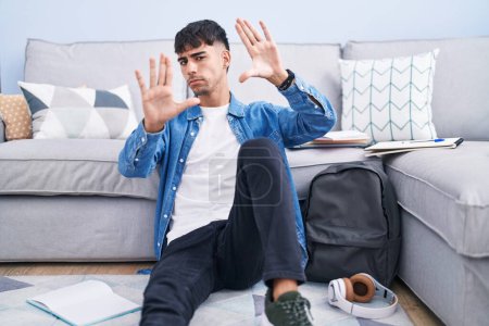 Foto de Hombre hispano joven sentado en el suelo estudiando para la universidad haciendo marco usando las manos palmas y los dedos, perspectiva de la cámara - Imagen libre de derechos