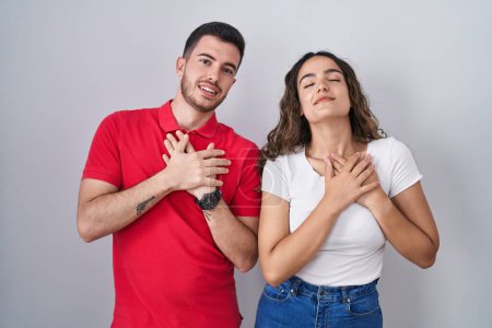 Téléchargez les photos : Jeune couple hispanique debout sur fond isolé souriant avec les mains sur la poitrine avec les yeux fermés et geste reconnaissant sur le visage. concept de santé. - en image libre de droit