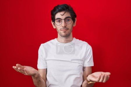 Photo for Young hispanic man standing over red background clueless and confused with open arms, no idea concept. - Royalty Free Image