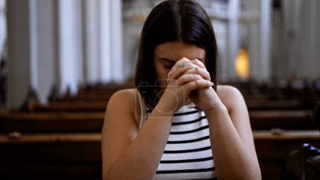 Photo for Young beautiful hispanic woman praying on a church bench at Augustinian Church in Vienna - Royalty Free Image