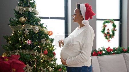 Foto de Mujer embarazada joven decorando el árbol de Navidad en casa - Imagen libre de derechos