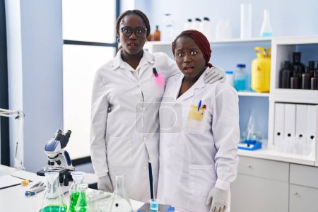 Photo for Two african women working at scientist laboratory scared and amazed with open mouth for surprise, disbelief face - Royalty Free Image