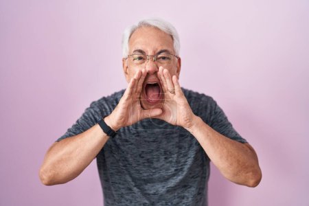 Téléchargez les photos : Homme d'âge moyen avec les cheveux gris debout sur fond rose criant en colère à haute voix avec les mains sur la bouche - en image libre de droit