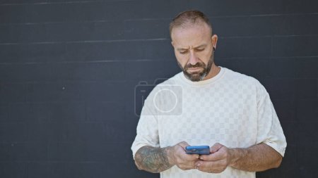 Foto de Joven guapo, absorto en la comunicación usando un teléfono inteligente sobre un fondo negro aislado, relajado pero serio - Imagen libre de derechos