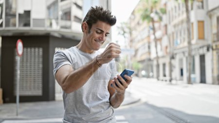 Téléchargez les photos : Jeune homme hispanique utilisant un smartphone célébrant dans la rue - en image libre de droit