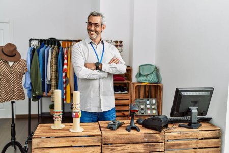 Téléchargez les photos : Homme d'âge moyen aux cheveux gris assistant de magasin debout avec les bras croisés geste au magasin de vêtements - en image libre de droit