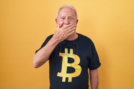 Téléchargez les photos : Homme âgé avec les cheveux gris portant Bitcoin t-shirt rire et rire embarrassé couvrant la bouche avec les mains, commérages et concept scandale - en image libre de droit