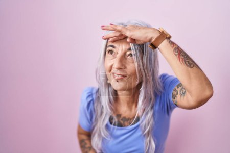 Photo for Middle age woman with tattoos standing over pink background very happy and smiling looking far away with hand over head. searching concept. - Royalty Free Image