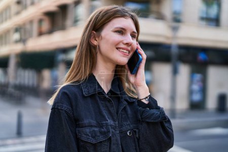 Photo for Young blonde woman smiling confident talking on the smartphone at street - Royalty Free Image