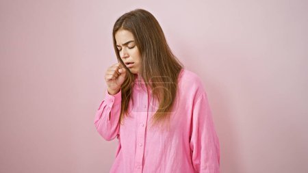 Photo for Stunning young hispanic woman, cool yet ill, coughing over a solitary pink backdrop. her beautiful hairstyle undone by flu; a portrait of sickness and strength. - Royalty Free Image