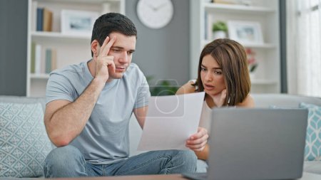 Photo for Beautiful couple using laptop reading document sitting on sofa at home - Royalty Free Image