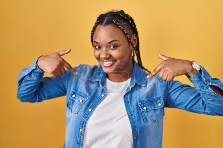 Photo for African american woman with braids standing over yellow background looking confident with smile on face, pointing oneself with fingers proud and happy. - Royalty Free Image