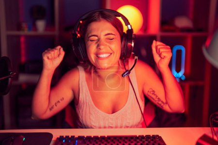 Téléchargez les photos : Jeune femme blonde jouant à des jeux vidéo portant un casque excité pour le succès avec les bras levés et les yeux fermés célébrant la victoire en souriant. concept gagnant. - en image libre de droit
