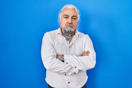 Photo for Middle age man with grey hair standing over blue background skeptic and nervous, disapproving expression on face with crossed arms. negative person. - Royalty Free Image
