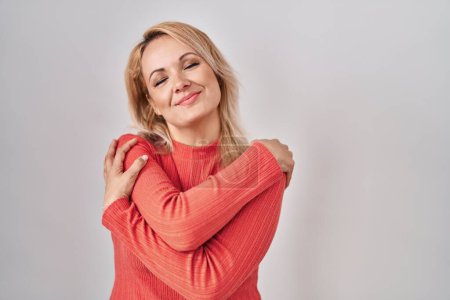 Téléchargez les photos : Femme blonde debout sur fond isolé se câlinant heureux et positif, souriant confiant. amour de soi et soins de soi - en image libre de droit