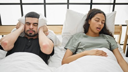 Téléchargez les photos : Stressé beau couple couvrant les oreilles de ronflement bruyant, couché ensemble au lit, inquiet de la question du sommeil dans leur chambre. - en image libre de droit