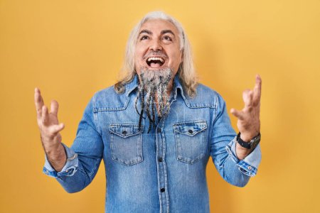 Photo for Middle age man with grey hair standing over yellow background celebrating mad and crazy for success with arms raised and closed eyes screaming excited. winner concept - Royalty Free Image