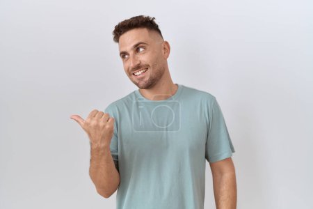 Téléchargez les photos : Hispanic man with beard standing over white background smiling with happy face looking and pointing to the side with thumb up. - en image libre de droit