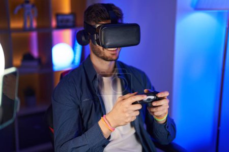 Téléchargez les photos : Jeune homme caucasien streamer jouer à un jeu vidéo en utilisant des lunettes de réalité virtuelle et joystick à la salle de jeu - en image libre de droit