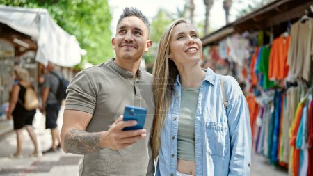 Foto de Hombre y mujer pareja sonriendo confiado usando teléfono inteligente en el mercado callejero - Imagen libre de derechos