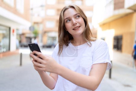 Foto de Joven mujer caucásica sonriendo confiado usando teléfono inteligente en la calle - Imagen libre de derechos