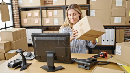 Téléchargez les photos : Jeune femme blonde commerce électronique travailleur d'affaires numérisation paquet au bureau - en image libre de droit