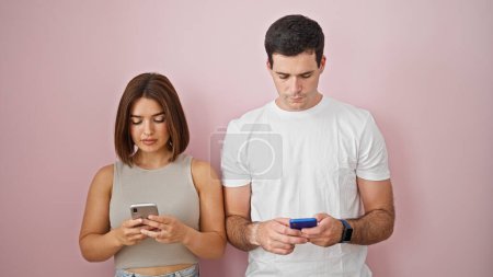 Téléchargez les photos : Beau couple utilisant des smartphones debout ensemble sur fond rose isolé - en image libre de droit
