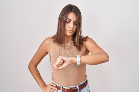 Téléchargez les photos : Jeune femme hispanique debout sur fond blanc vérifier l'heure sur la montre-bracelet, détendu et confiant - en image libre de droit