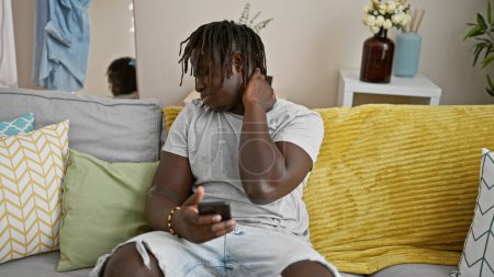 Foto de Hombre afroamericano usando teléfono inteligente que sufre de dolor cervical en casa - Imagen libre de derechos