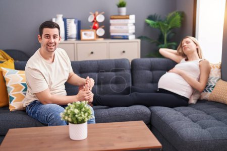 Téléchargez les photos : Homme et femme couple baisers ventre assis sur canapé à la maison - en image libre de droit