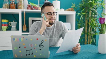 Photo for Hispanic man talking on the phone reading document at dinning room - Royalty Free Image