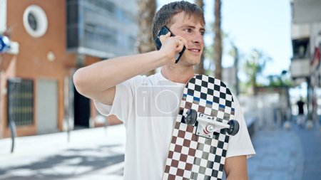 Téléchargez les photos : Jeune homme caucasien parlant sur smartphone tenant patiner à la rue - en image libre de droit