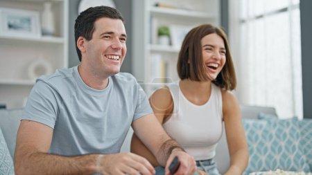 Photo for Beautiful couple watching tv sitting on sofa at home - Royalty Free Image
