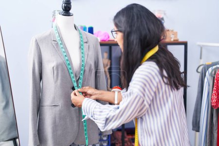 Téléchargez les photos : Young beautiful hispanic woman tailor measuring jacket at clothing factory - en image libre de droit