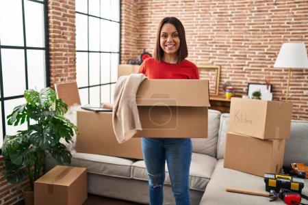 Photo for Young beautiful hispanic woman smiling confident holding package with clothes at new home - Royalty Free Image