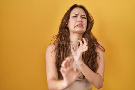 Photo for Young hispanic woman standing over yellow background disgusted expression, displeased and fearful doing disgust face because aversion reaction. with hands raised - Royalty Free Image