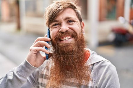 Téléchargez les photos : Jeune rousse homme souriant confiant parler sur le smartphone à la rue - en image libre de droit